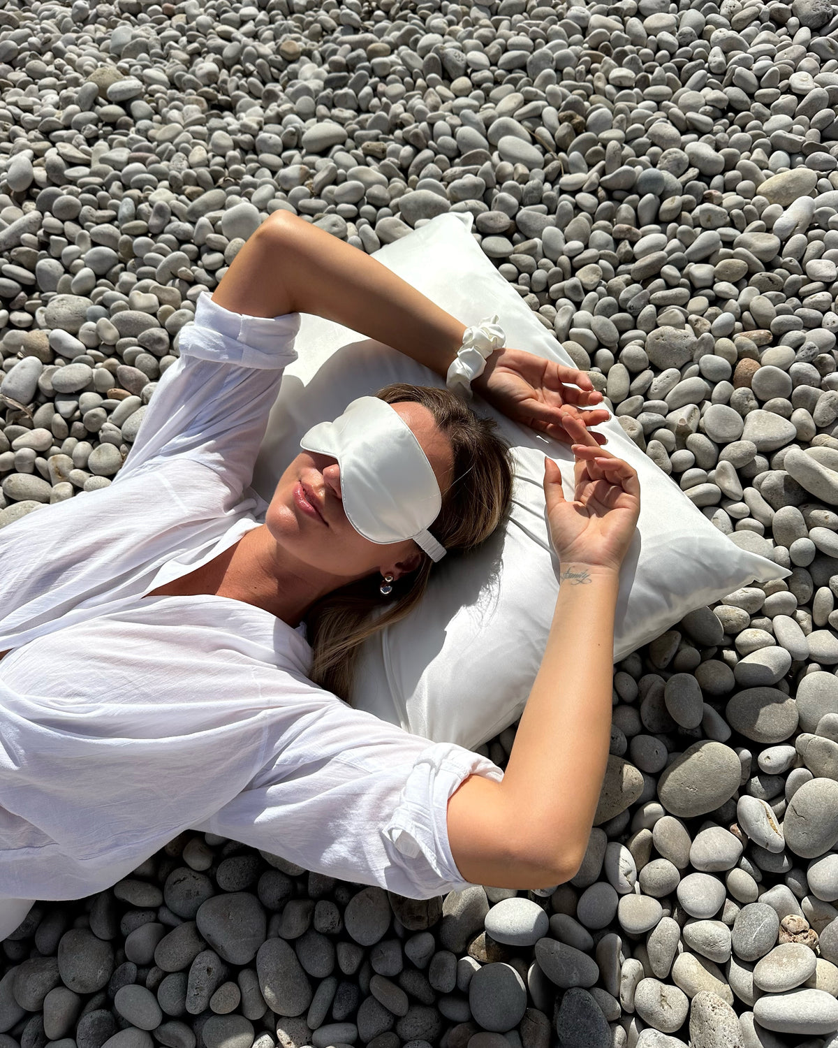taie d'oreiller en soie blanche ivoire Sisilk utilisée par une femme sur une plage méditerranéenne pour protéger les cheveux et la peau pendant le sommeil.