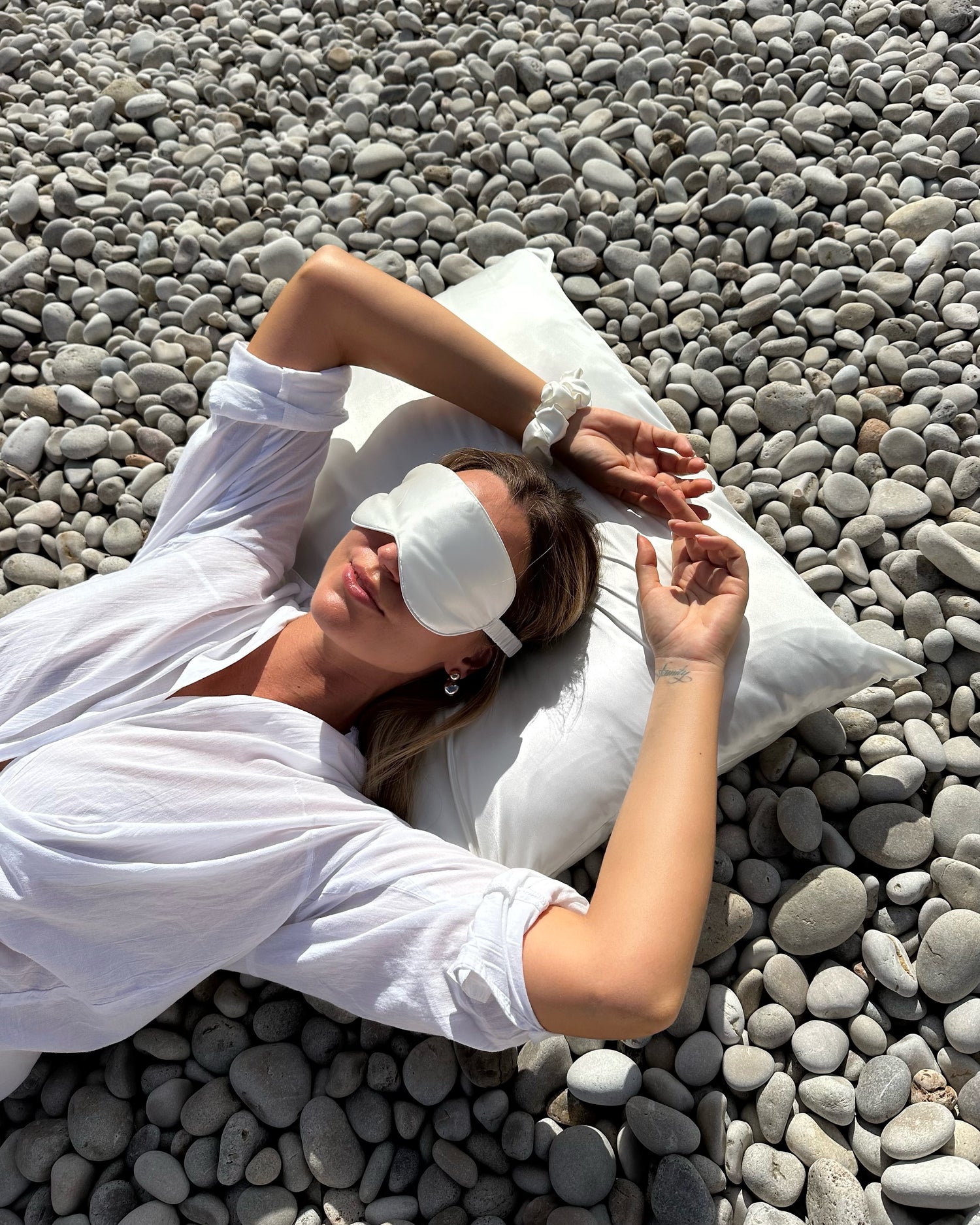 taie d'oreiller en soie blanche ivoire Sisilk utilisée par une femme sur une plage méditerranéenne pour protéger les cheveux et la peau pendant le sommeil.